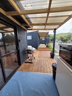 A covered outdoor area with a wooden deck, a grill, and a stroller. - Camping & Caravan Spots
Open Spaces to camp
 (Pōrangahau)