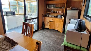 Cocina compacta con armarios de madera, microondas, refrigerador y comedor con mesa y sillas.