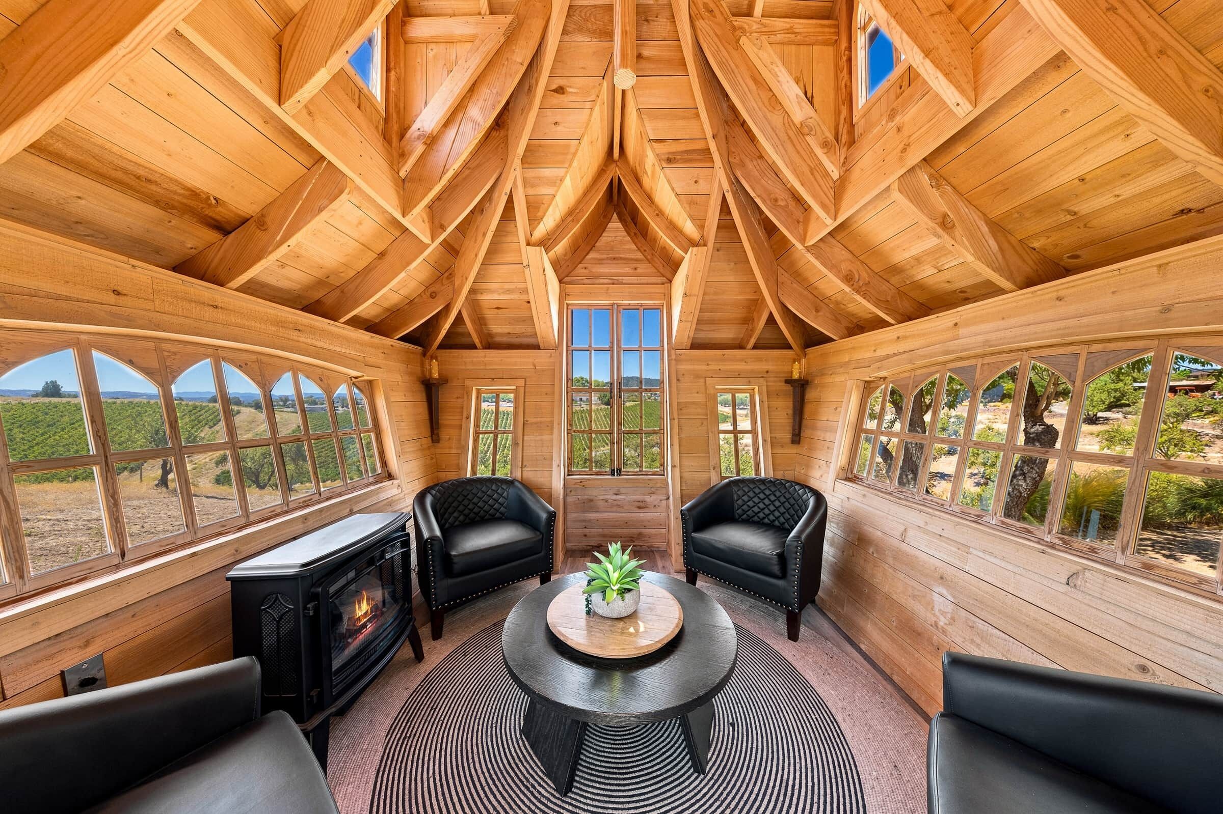 Ein Holzkaminzimmer mit Kamin, zwei Ledersesseln, einem runden Tisch mit Pflanze und großen Fenstern mit Blick ins Freie.