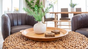 Una zona de estar acogedora con una mesa redonda de madera, un jarrón blanco con follaje verde y dos sofás de cuero marrón.