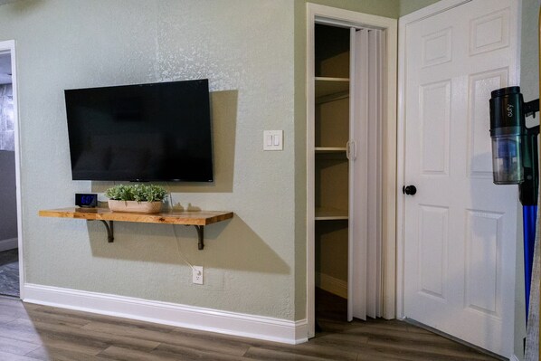 A room with a mounted television, a shelf with a plant, and a closed door.