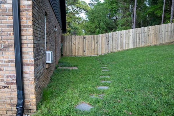 A brick building with a wooden fence, a grassy yard, and a paved path.
