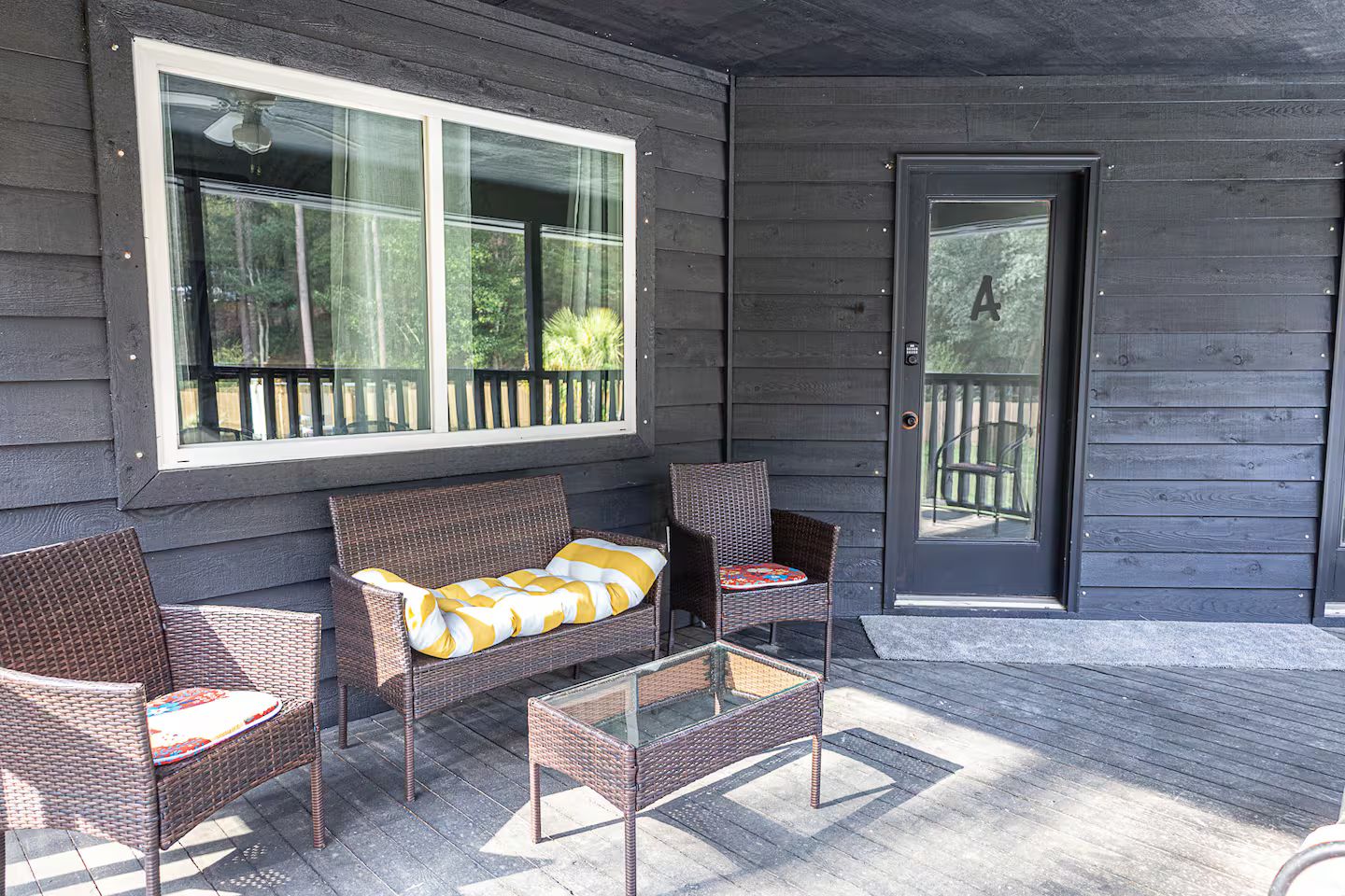 A porch with wicker furniture, a glass table, and a door leading to a deck.