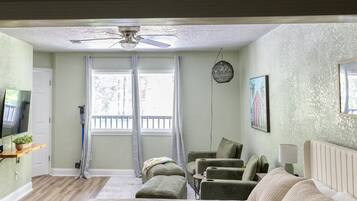 A room with a ceiling fan, a television, a window with curtains, a sofa, and a chair.