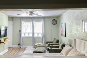 A room with a ceiling fan, a television, a window with curtains, a sofa, and a chair.
