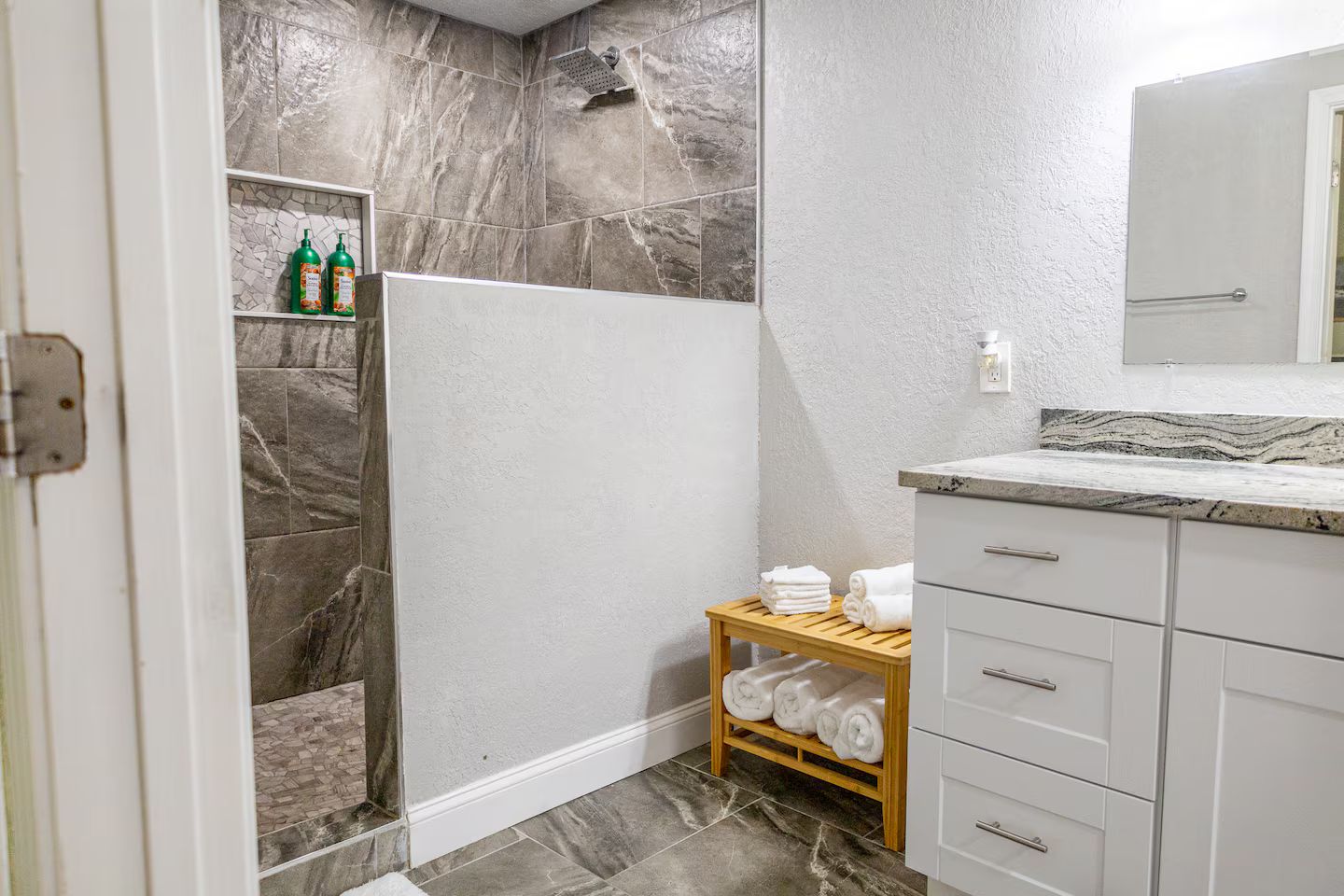 Un baño con ducha, un lavamanos con encimera de mármol y un perchero con toallas.