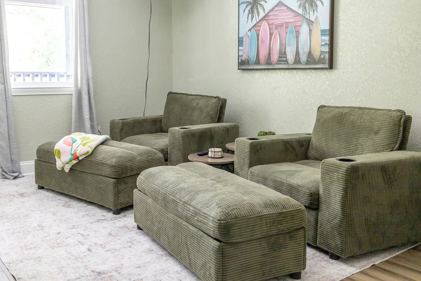 A room with a sectional sofa set, a small round table, and a painting of surfboards on the wall.