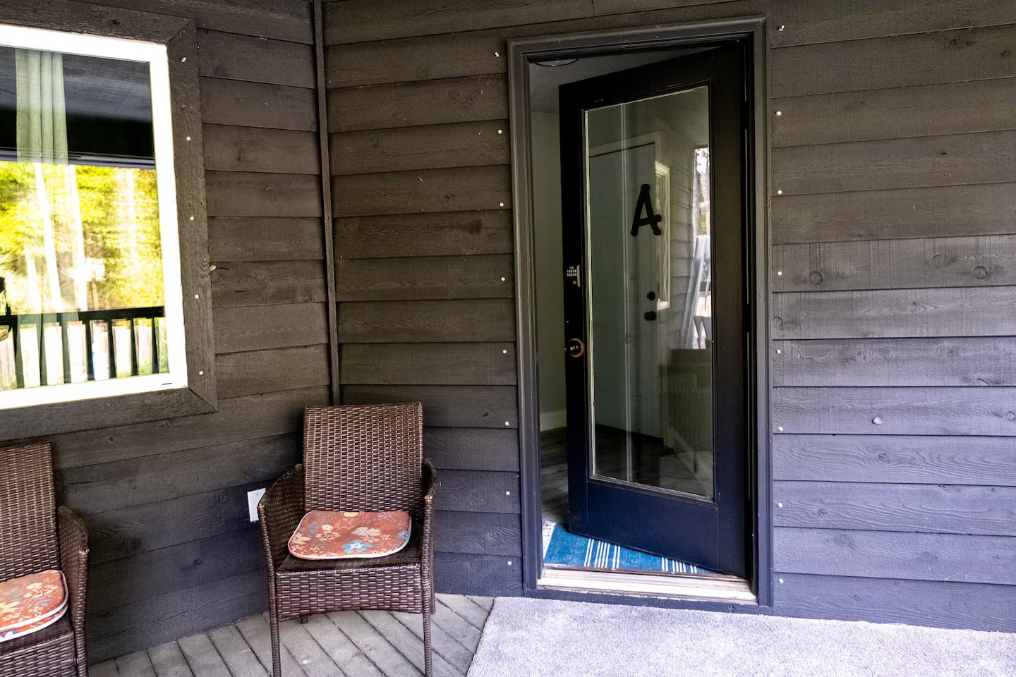 A wooden exterior with a glass door marked with the letter 'A' and two wicker chairs outside.