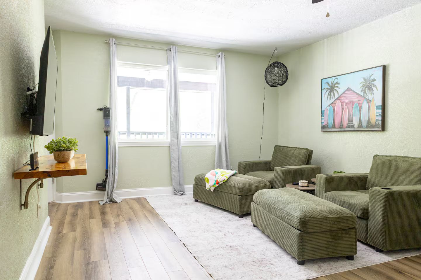 Un salon comprenant un canapé d’angle, un téléviseur à écran plat fixé au mur, une plante en pot et un tableau représentant des planches de surf.