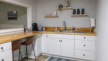 Eine kompakte Küche mit weißen Schränken, einer Holz Arbeitsplatte, einer Kaffeemaschine und einem Barhocker.