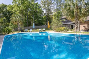 A rectangular swimming pool with a clear blue surface, surrounded by trees and a wooden deck with lounge chairs.