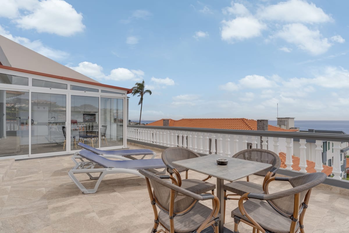 A terrace with a table and chairs, a sun lounger, and a glass-enclosed kitchen area.