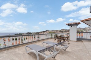 Una terraza con dos tumbonas, una mesa con sillas y vistas al mar y al pueblo.