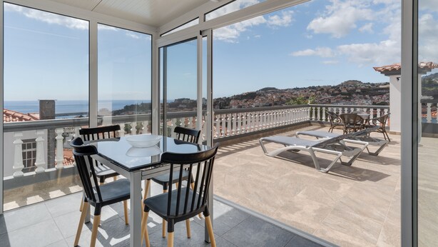 A balcony with a table and chairs, a view of the sea and a town, and a tiled floor. - Villa Winter (Funchal)
