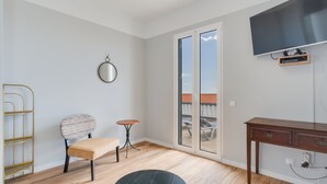 A modern room with a wooden floor, a round table, a chair, a small table, a desk, a television, and a sliding glass door leading to an outdoor area. - Villa Winter (Funchal)