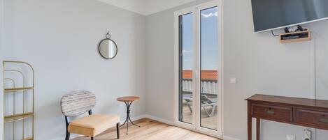 Una habitación moderna con suelo de madera, una mesa redonda, una silla, una mesita, un escritorio, un televisor y una puerta corrediza de vidrio que da a un espacio exterior.