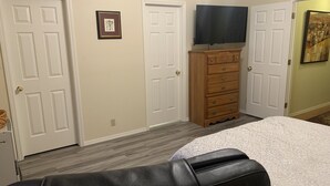 Un dormitorio con cama, cómoda, televisor y dos puertas.