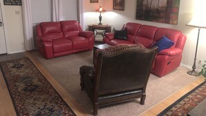 Una sala de estar con dos sofás de cuero rojo, una silla de madera oscura, un tapete estampado, una mesita con una lámpara y un cuadro en la pared.