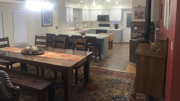 Una cocina moderna con armarios blancos, una isla central y una zona de comedor con muebles de madera y una alfombra estampada.