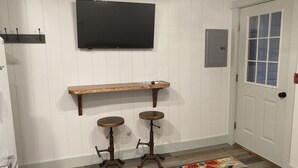 Een gang met een houten bankje, twee krukken, een tv aan de muur en een tapijt met een patroon.