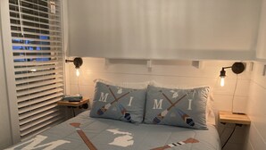 Een slaapkamer met een bed, twee kussens met een ijshockeythema, een nachtkastje, een lamp en een raam met jaloezieën.