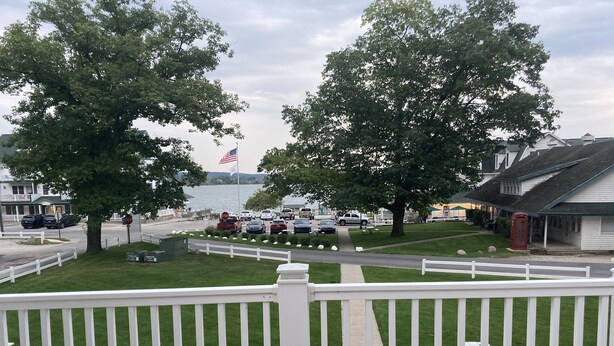 Een pand aan het water met een terras, witte picket fence en uitzicht op het water en geparkeerde auto's.