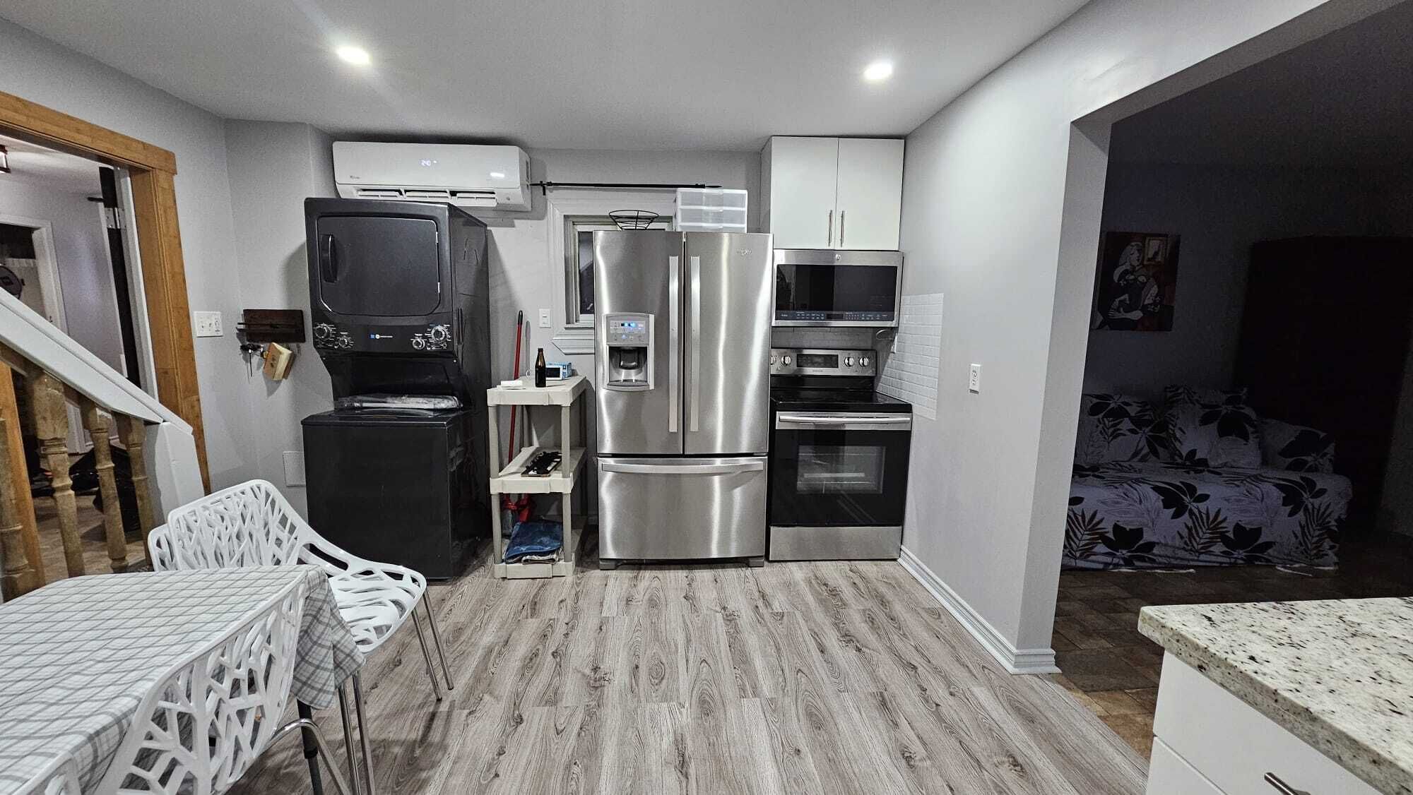 Cocina compacta con refrigerador, microondas, horno y un pequeño comedor con mesa y sillas.