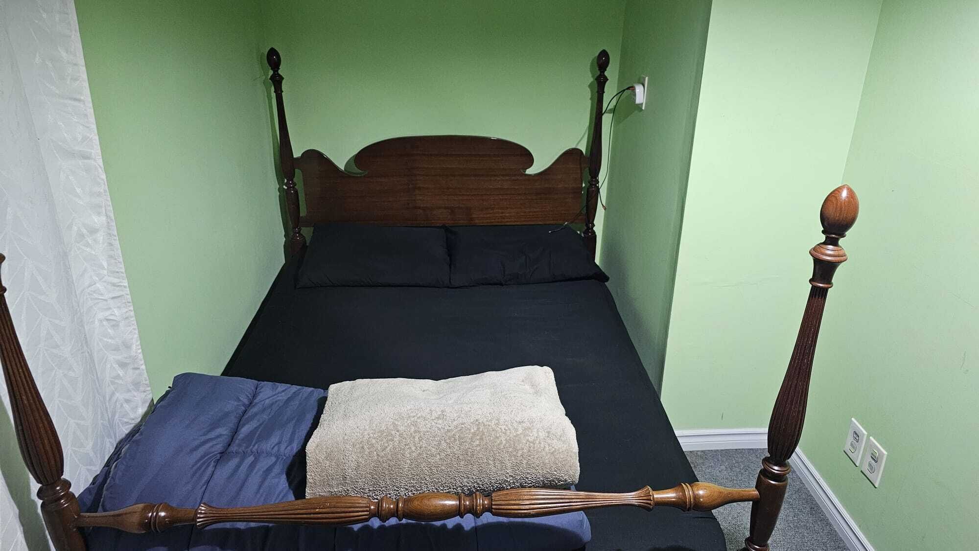 Una cama individual con cabecera de madera y cuatro pilares, una manta azul y una almohada color beige.