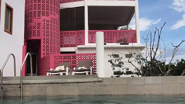 Een zwembadgedeelte met een modern gebouw, een roze gevel en een helderblauwe lucht.