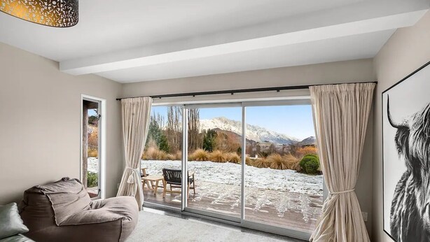 A modern living room with a large sliding glass door leading to a snowy outdoor area, a sofa, and a dining table with chairs. - Mountain View Villa - Rural Retreat (Hot Tub, Tennis, Petanque, Putting Green) (Queenstown)
