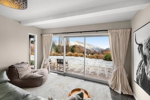 A modern living room with a large sliding glass door leading to a snowy outdoor area, a sofa, and a dining table with chairs.