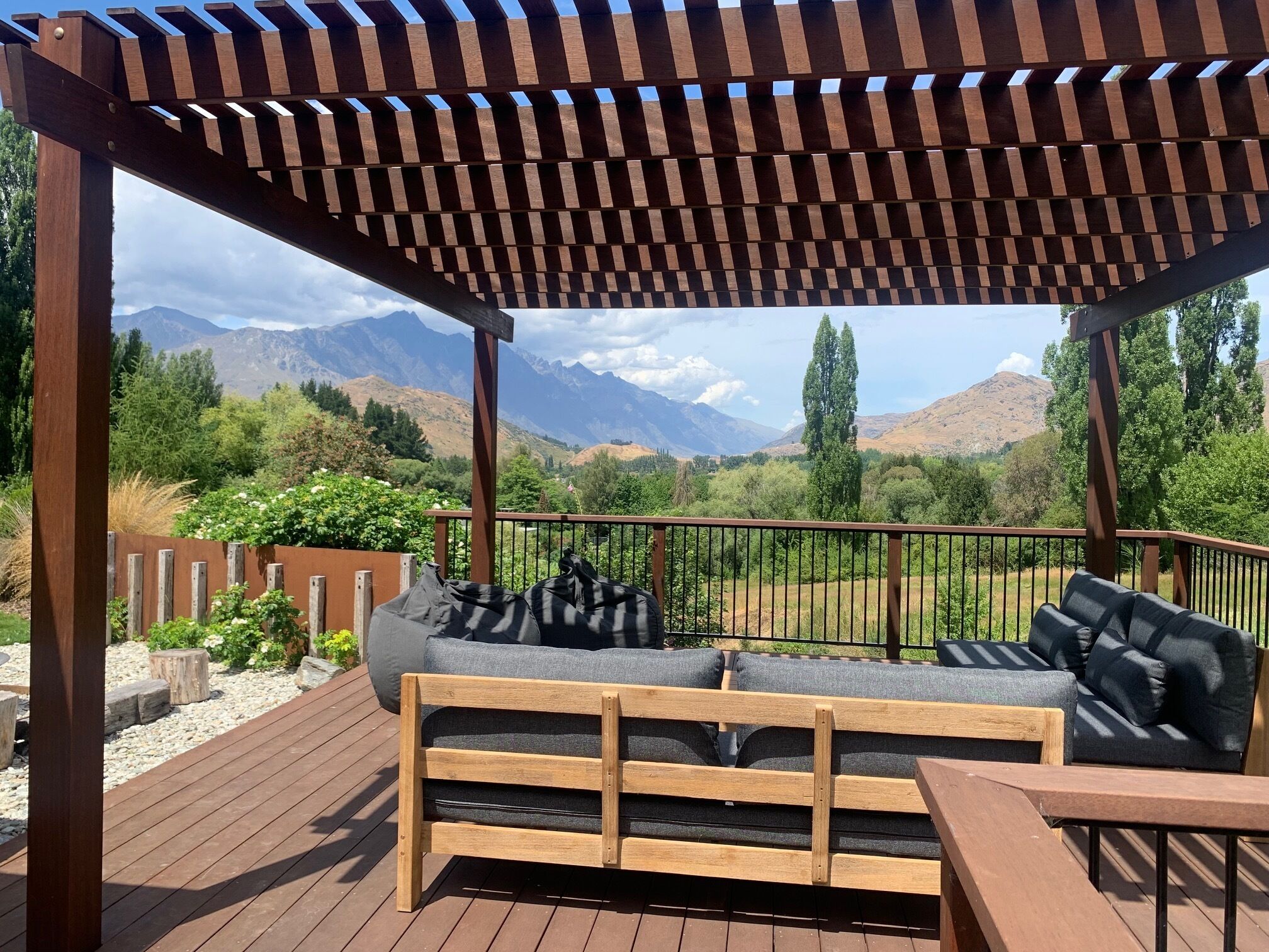 Een houten terras met een pergola, een bank en uitzicht op bergen.