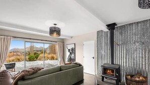 A modern living room with a sofa, a fireplace, and a large window overlooking a snowy landscape. - Mountain View Villa - Rural Retreat (Hot Tub, Tennis, Petanque, Putting Green) (Queenstown)