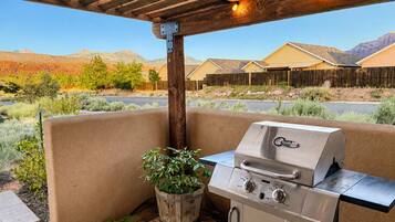 Une terrasse extérieure dotée d’un barbecue intégré, d’une pergola en bois au-dessus et offrant une vue sur un quartier résidentiel, avec des maisons et des montagnes en arrière-plan.
