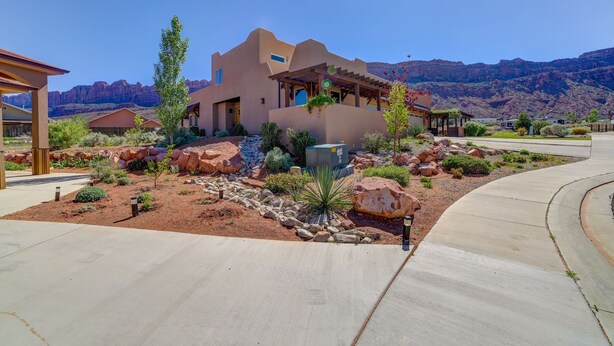 A modern house with a patio, surrounded by desert landscaping and mountains in the background.