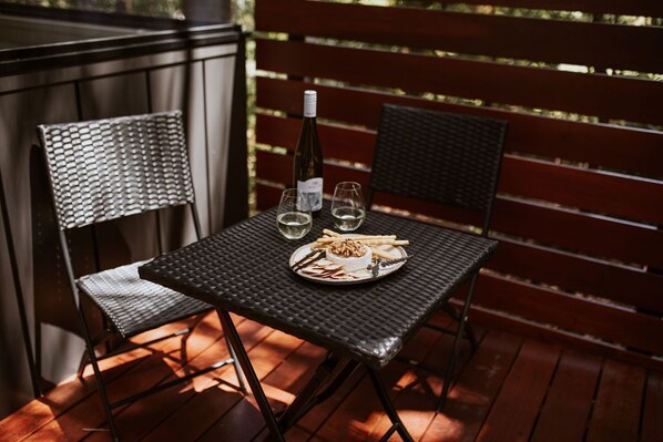 A table with a bottle of wine, two glasses, and a plate of food on a deck. - Custom Designed Tiny Home (Ulladulla)