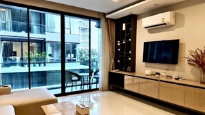 A modern living room with a large TV, a sofa, a coffee table, and a balcony with outdoor furniture. - The Star Hill  (Chiang Mai)