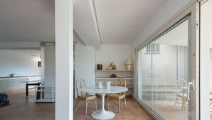 Ein modernes Interieur mit einem runden Tisch und Stühlen, einem weißen Schrank und einer Glastür zu einem Außenbereich.