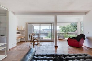 A spacious living area with a sofa, a dining table with chairs, a red chair, and a view through a glass door. - Popolo Luxury Penthouse Garden (Roma)