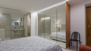 Ein Schlafzimmer mit Bett, Stuhl, Spiegel, Kleiderschrank und Duschbereich.