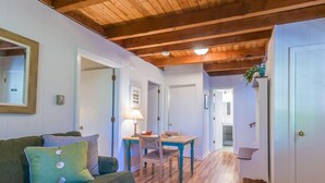 Una sala de estar acogedora con techo de madera, un sofá verde, una mesa de comedor con sillas y un pasillo que conduce a una puerta.