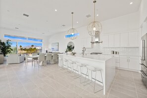 A modern kitchen with white cabinetry, a large island with bar stools, and pendant lighting.