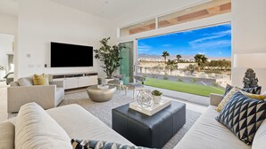 Un salon moderne doté d’un grand téléviseur, de sièges confortables, d’une table basse et offrant une vue sur un jardin aménagé.