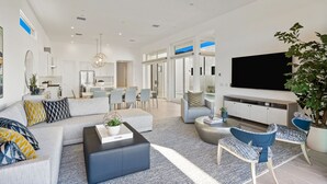 Un salon moderne avec un canapé, une table basse et un meuble pour la télévision. On aperçoit un coin repas avec des chaises et, au fond, une cuisine.