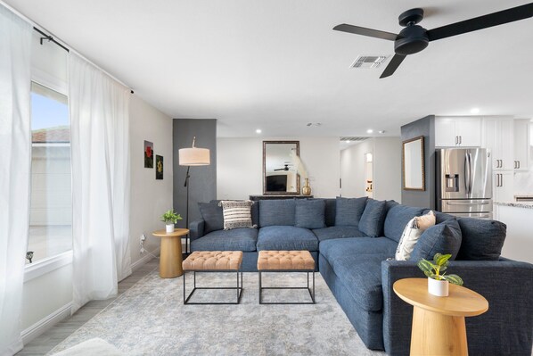 A modern living room with a sectional sofa, ottomans, a small side table, and a ceiling fan.