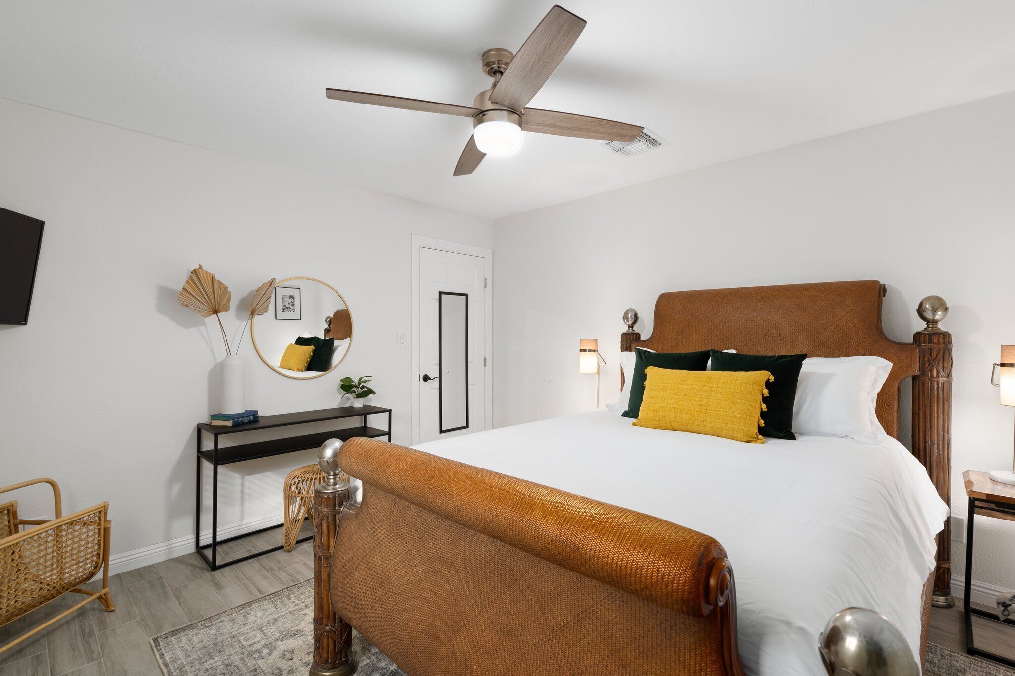 Une chambre d’hôtel équipée d’un lit, d’un bureau, d’une chaise, d’un ventilateur de plafond et d’un téléviseur fixé au mur.