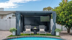 Un espacio al aire libre cubierto con dos sillas, una mesa, una piscina y plantas en macetas.