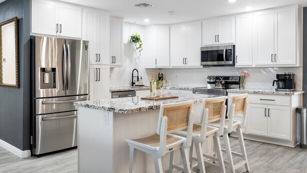 Una cocina moderna con armarios blancos, electrodomésticos de acero inoxidable e isla de mármol con taburetes.