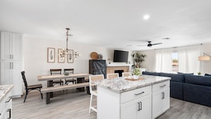 Una cocina moderna con armarios blancos, una isla con encimera de granito y un comedor con sillas y banco de madera.