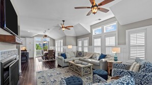 A spacious living area with a fireplace, ceiling fans, and a large window. - 4919-The Leonardo - Soundside Oasis | Pool, Hot Tub & Fire Pit (Kitty Hawk)